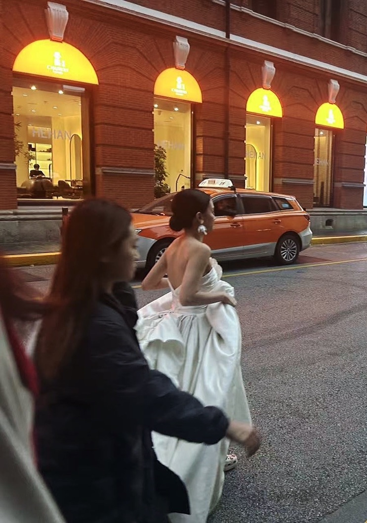 红砖建筑与出租车前，身穿婚纱的人走过街头
