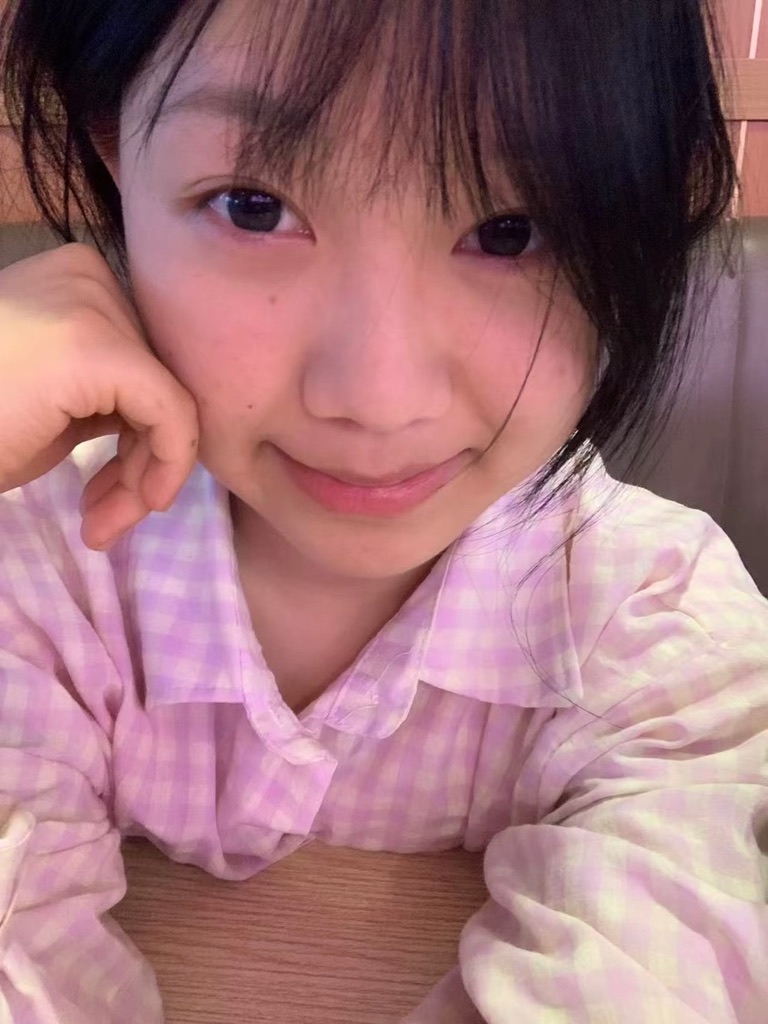 身穿浅紫格纹上衣的人倚着桌面微笑